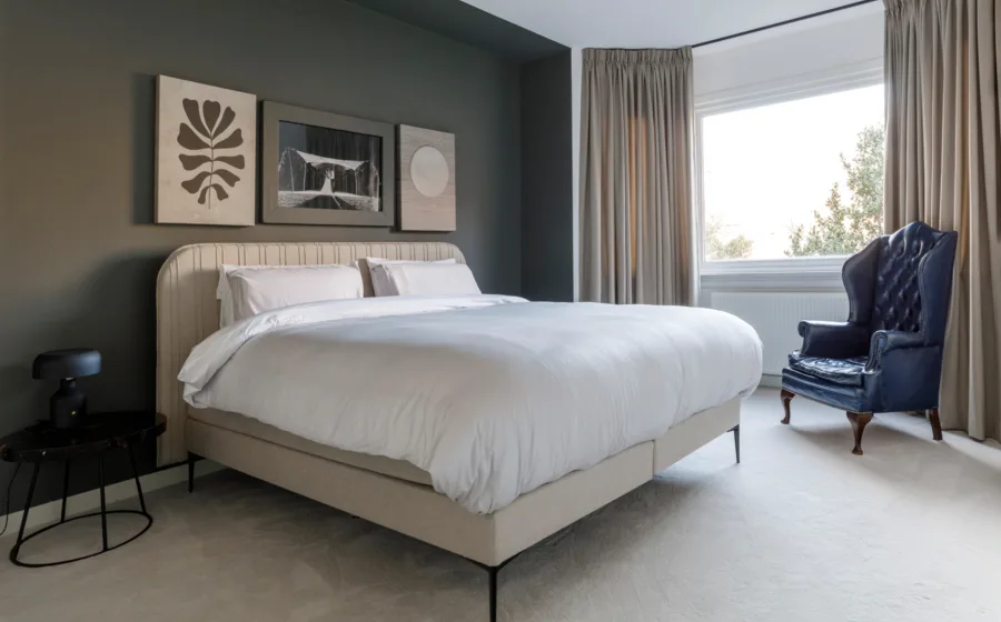 Slaapkamer met beige tapijt en natuurlijke wanddecoratie en een bed op metalen bedframe.