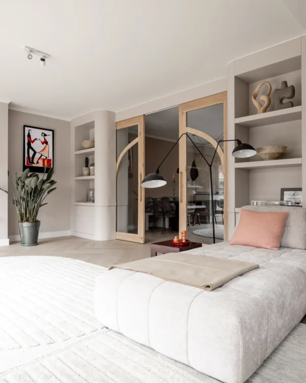 Zonnige woonkamer met gebogen houten deuren met glas en Art Nouveau boekenkasten in natuurlijke kleuren.