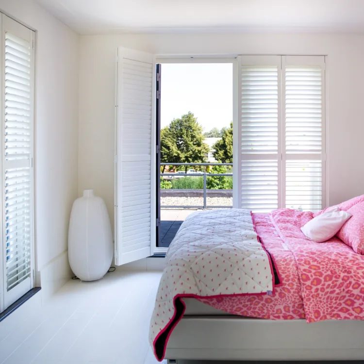 Slaapkamer in witte en lichte tinten met grote ramen en deur met witte houten shutters